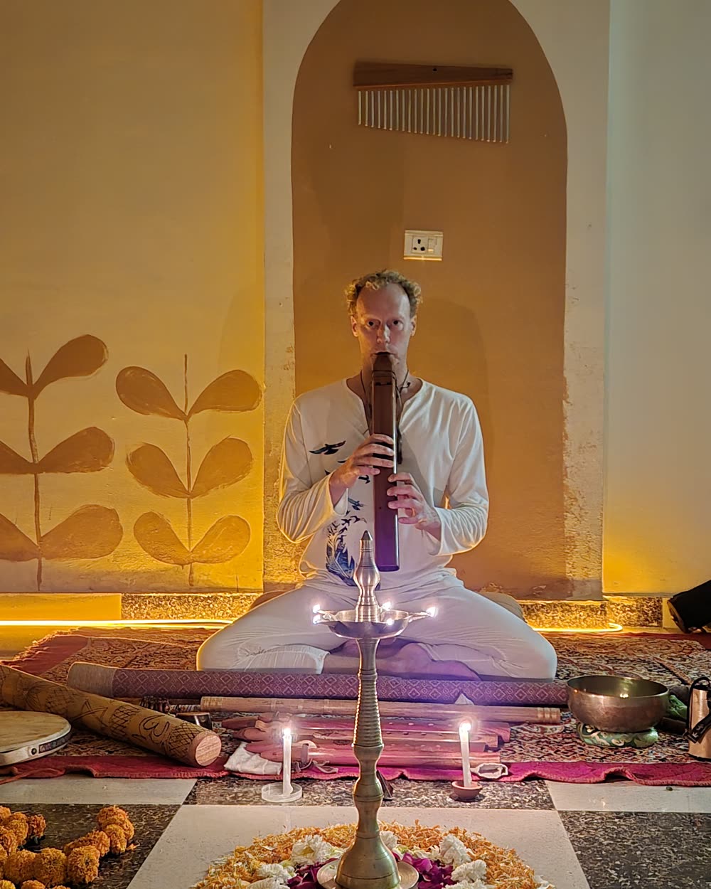 Tomas playing a flute in front of a candlelit ceremony altar with flowers