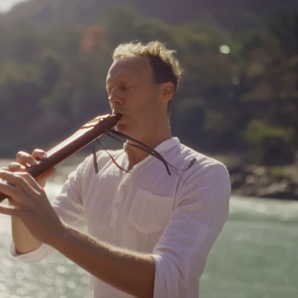 Tomas playing a wooden flute by a sunlit river