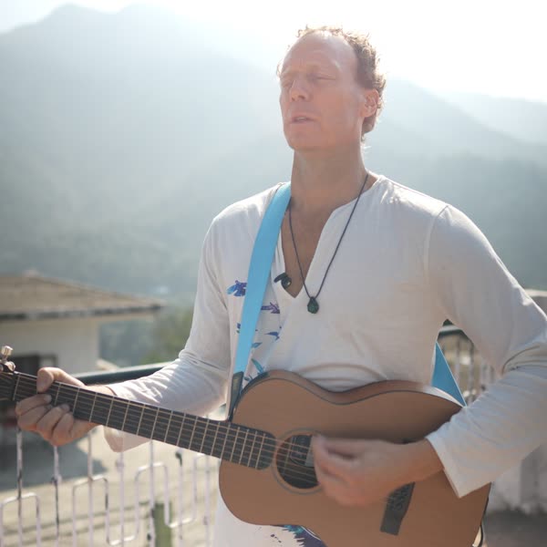 Tomas playing acoustic guitar on a rooftop with mountains behind