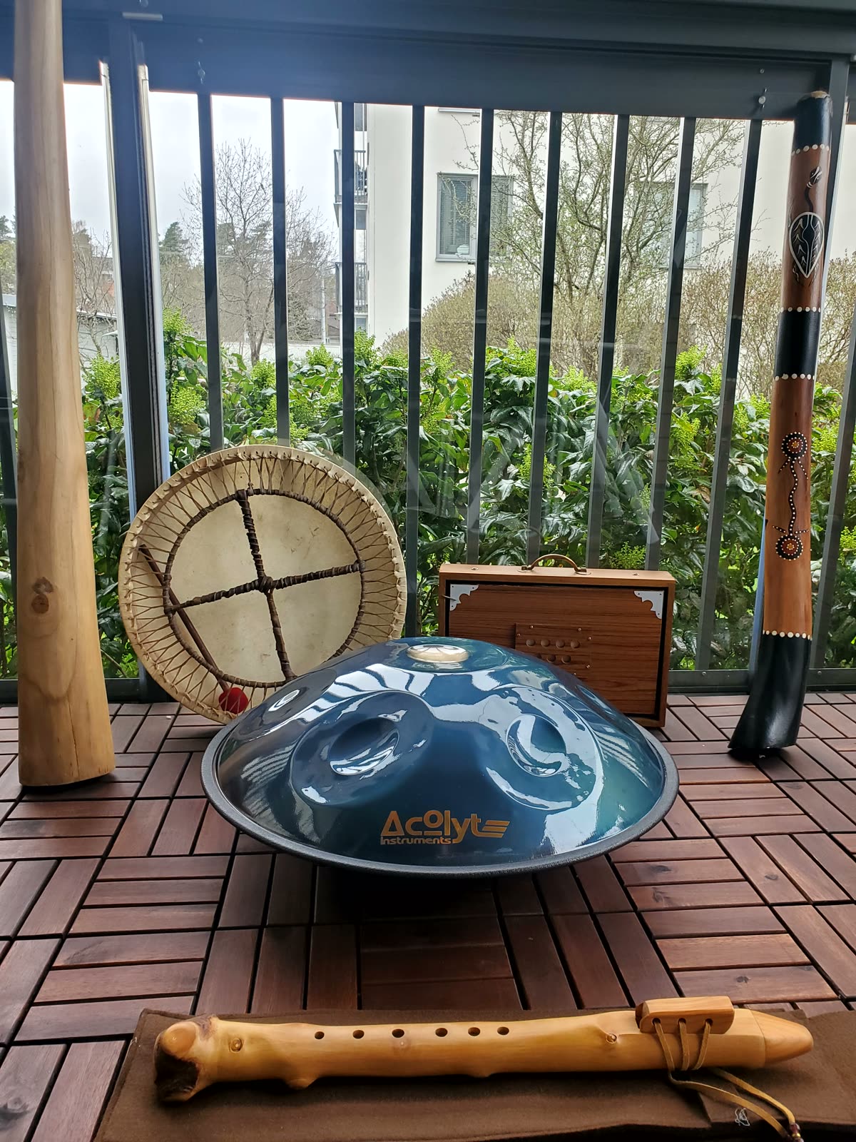 Handpan, frame drum, didgeridoo and flute laid out on a wooden balcony