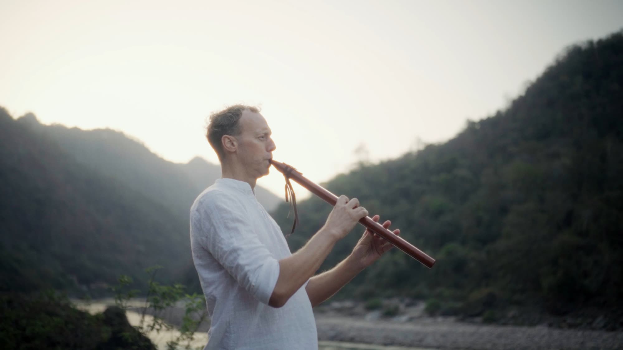 Tomas Stendahl playing a wooden flute by a mountain river at dusk